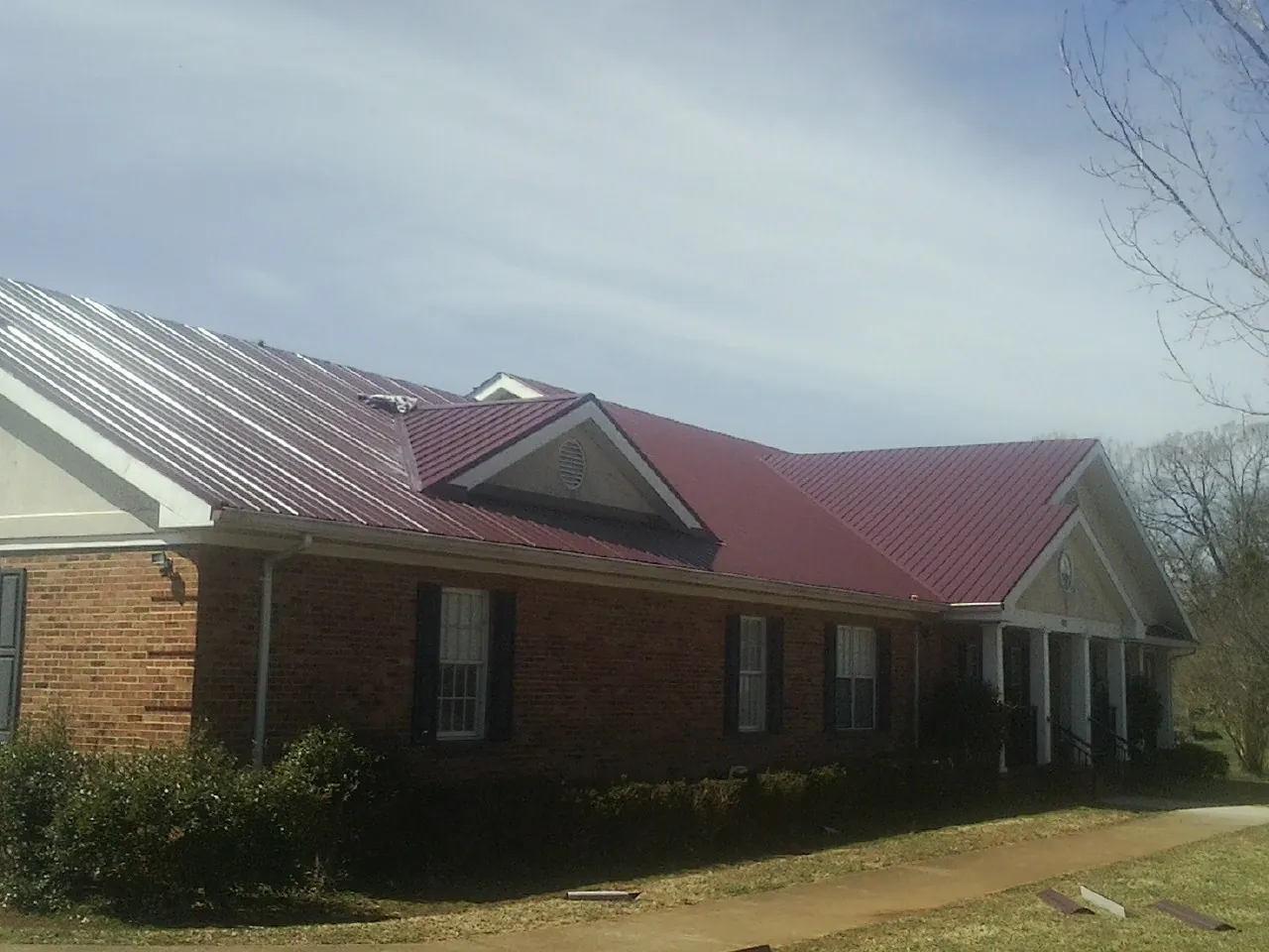 Red metal roof with gabled entries on a long brick building, from a Hail Damage Roof Repair job in Cataula