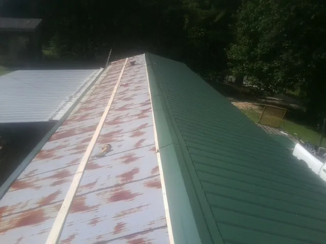 Old rusted panels beside newly installed green metal roofing — Wind Damage Roof Repair by Roofing Brothers in Cataula