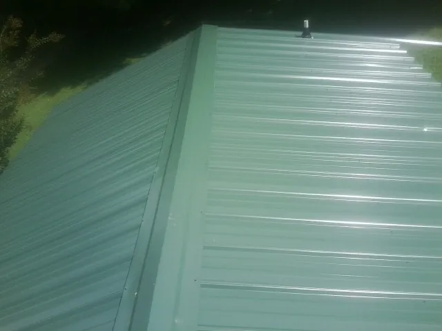 New green metal panels meeting at the ridge of a roof — Flat Roof Repair work by our crew in Cataula