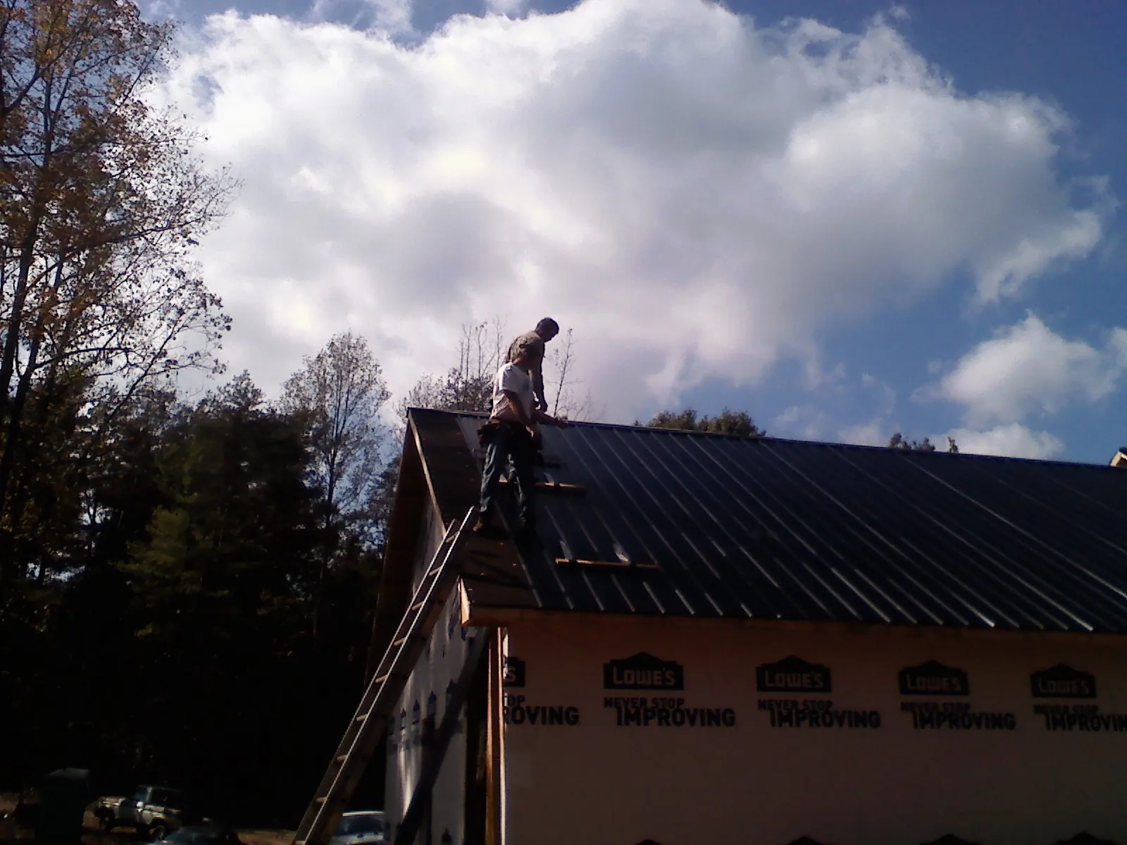 Roofer fastening dark metal panels high against a cloudy sky in Cataula