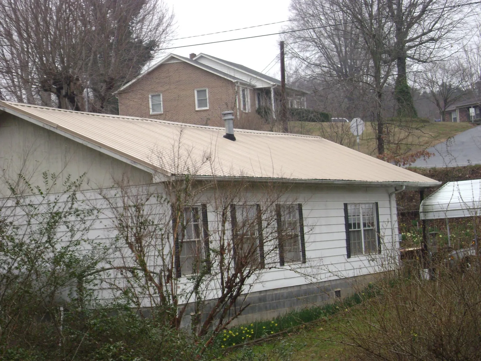 Tan metal roof on a white sided house set into a hillside — Commercial Roofing by Roofing Brothers in Cataula